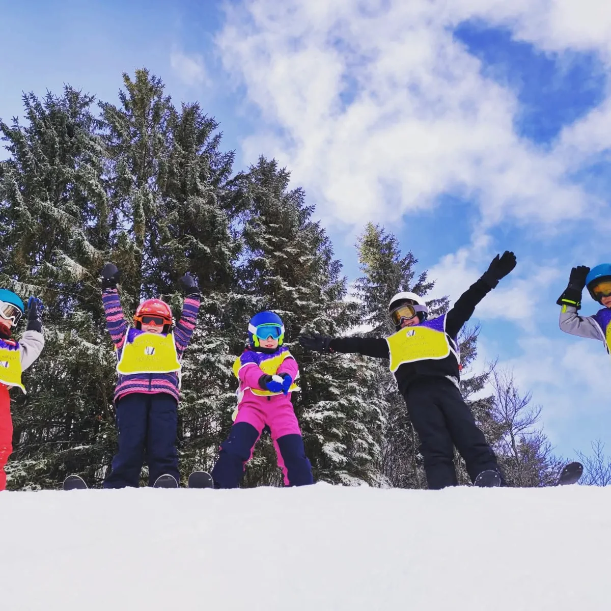 Des enfants Moonshot lèvent les bras sur la neige, devant les sapins