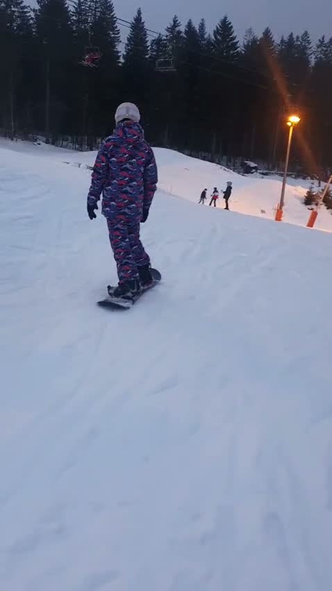 Une snowboardeuse descend une piste en fin de journée
